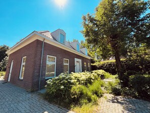 A two-story brick house with a visible chimney, a paved driveway, and a large tree to the right. - New Listing (Zeewolde)