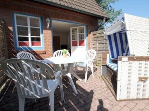 A patio with a table and chairs, a wicker sofa, and a brick house with blue trim. - Badestrasse 40a - Holiday Apartment 1 (Wyk auf Foehr)