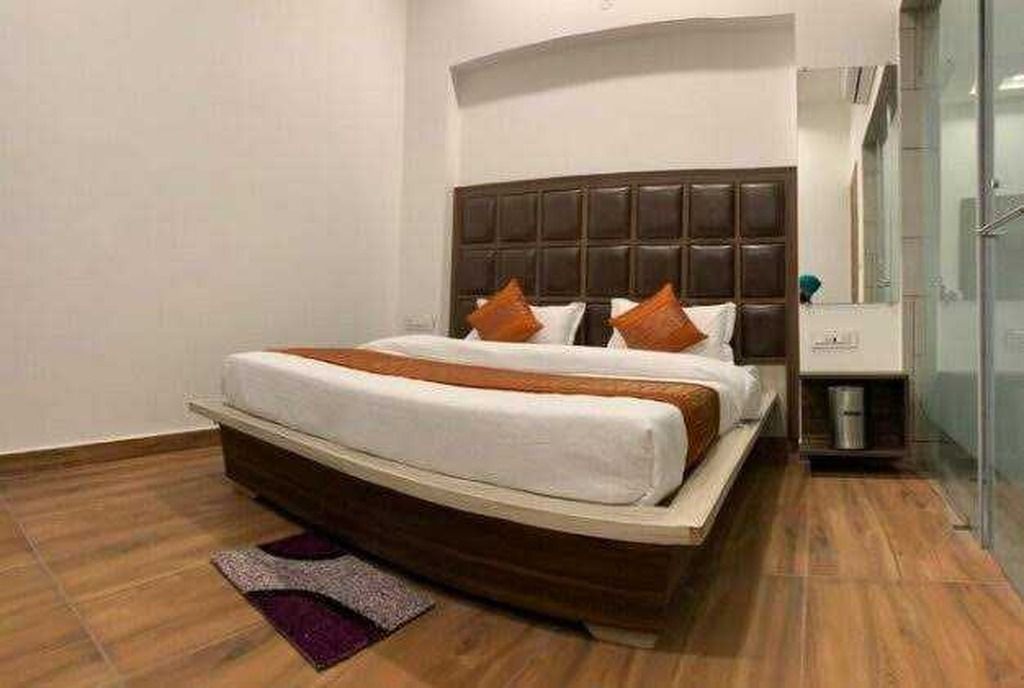 A hotel room with a large bed, a wooden floor, a bathroom with a glass shower, and a small trash bin.
