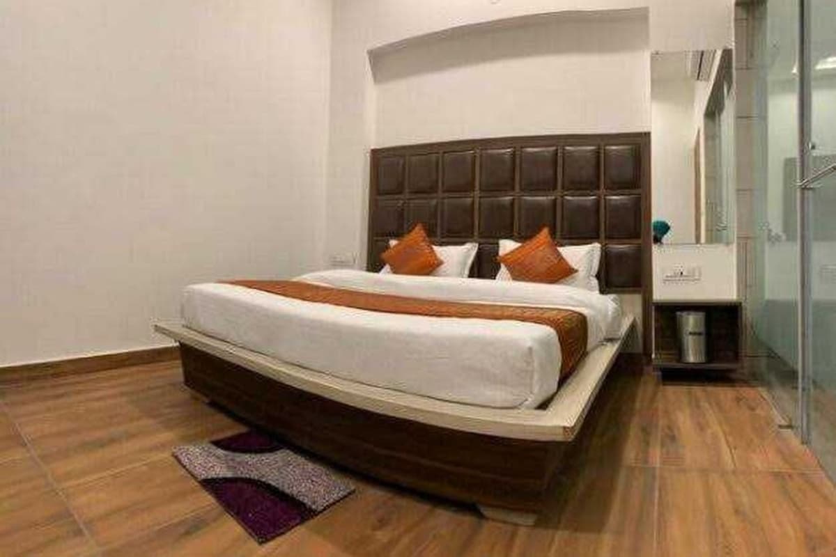 A hotel room with a large bed, a wooden floor, a bathroom with a glass shower, and a small trash bin.