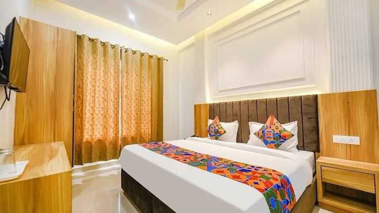 A hotel room with a large bed, a wooden headboard, a bedside table, and a TV mounted on the wall.