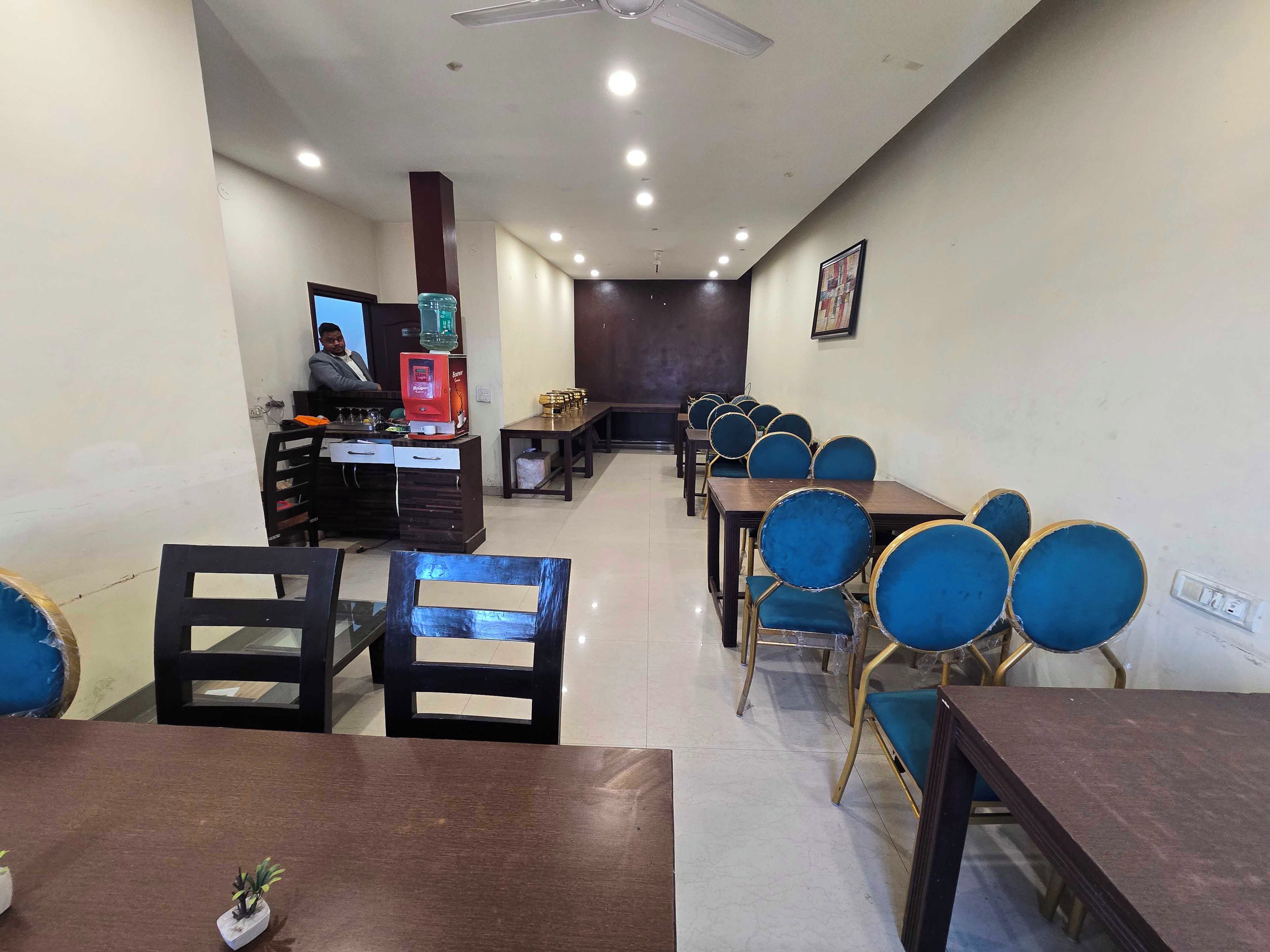A conference room with multiple tables and chairs, a coffee machine, and a counter with a computer.