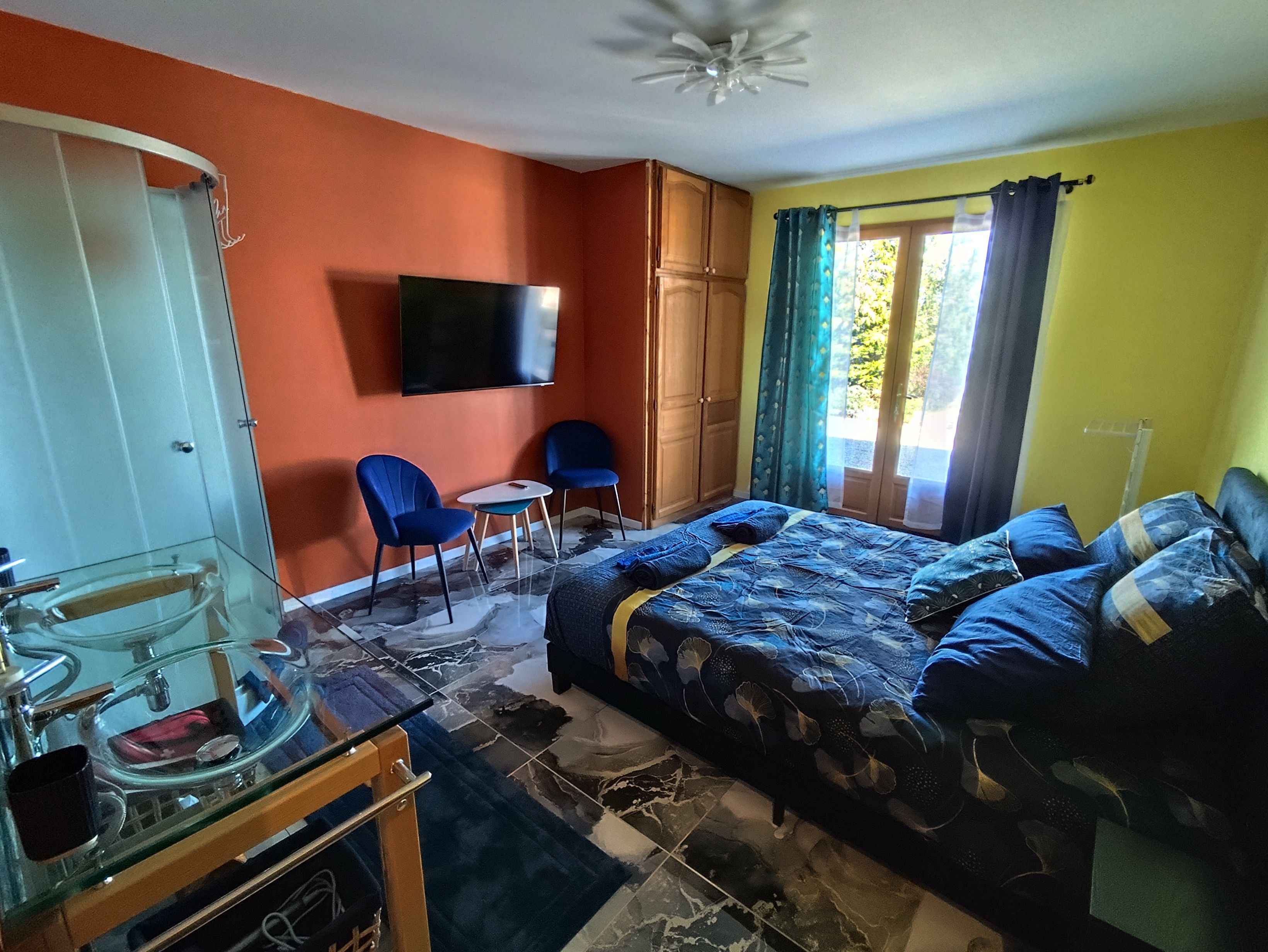 A bedroom with a bed, a TV, a chair, a small table, and a window with curtains.
