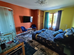 Une chambre à coucher avec un lit, une télévision, une chaise, une petite table et une fenêtre avec des rideaux.