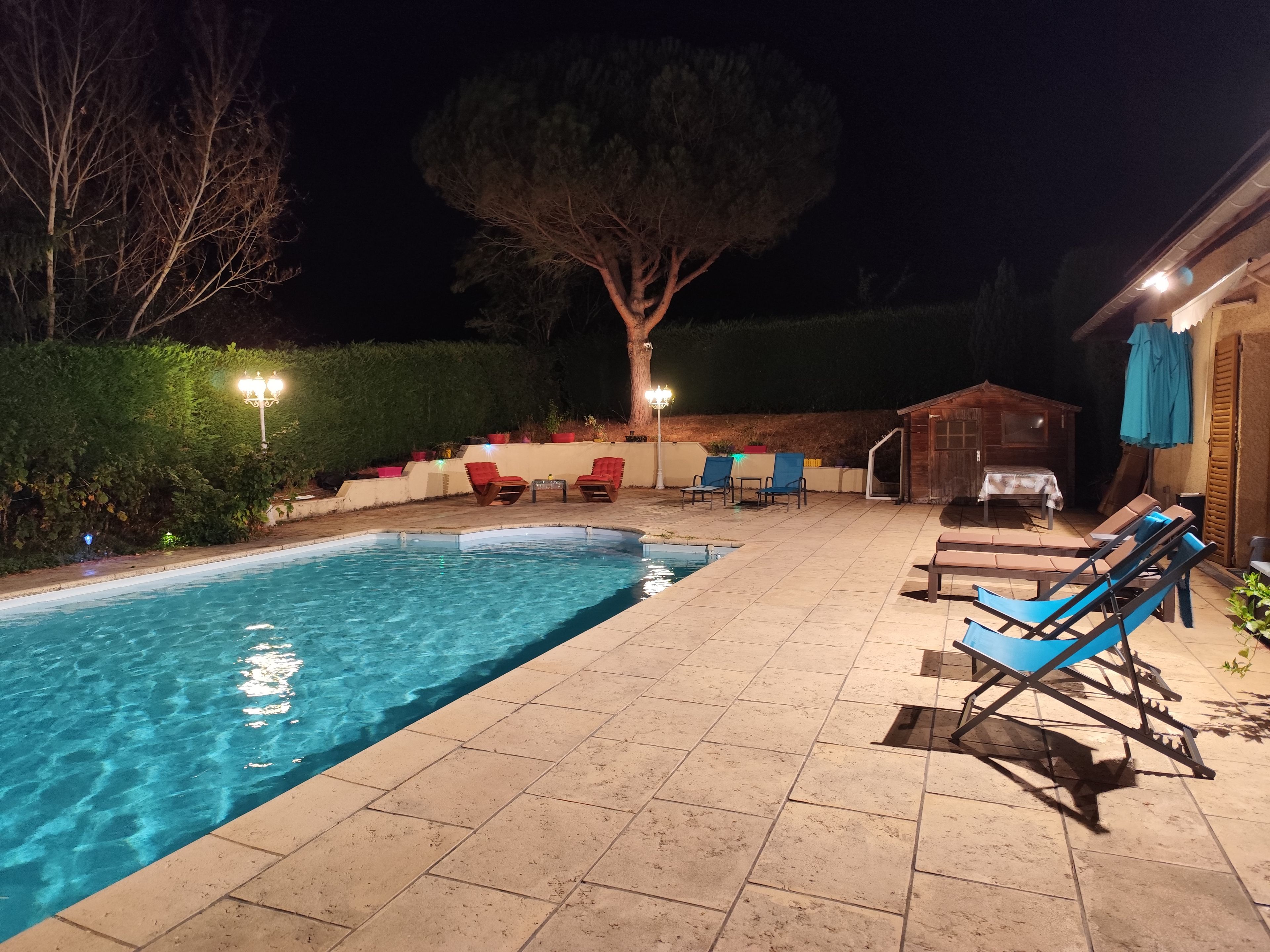 A swimming pool with lounge chairs and a barbecue area at night.