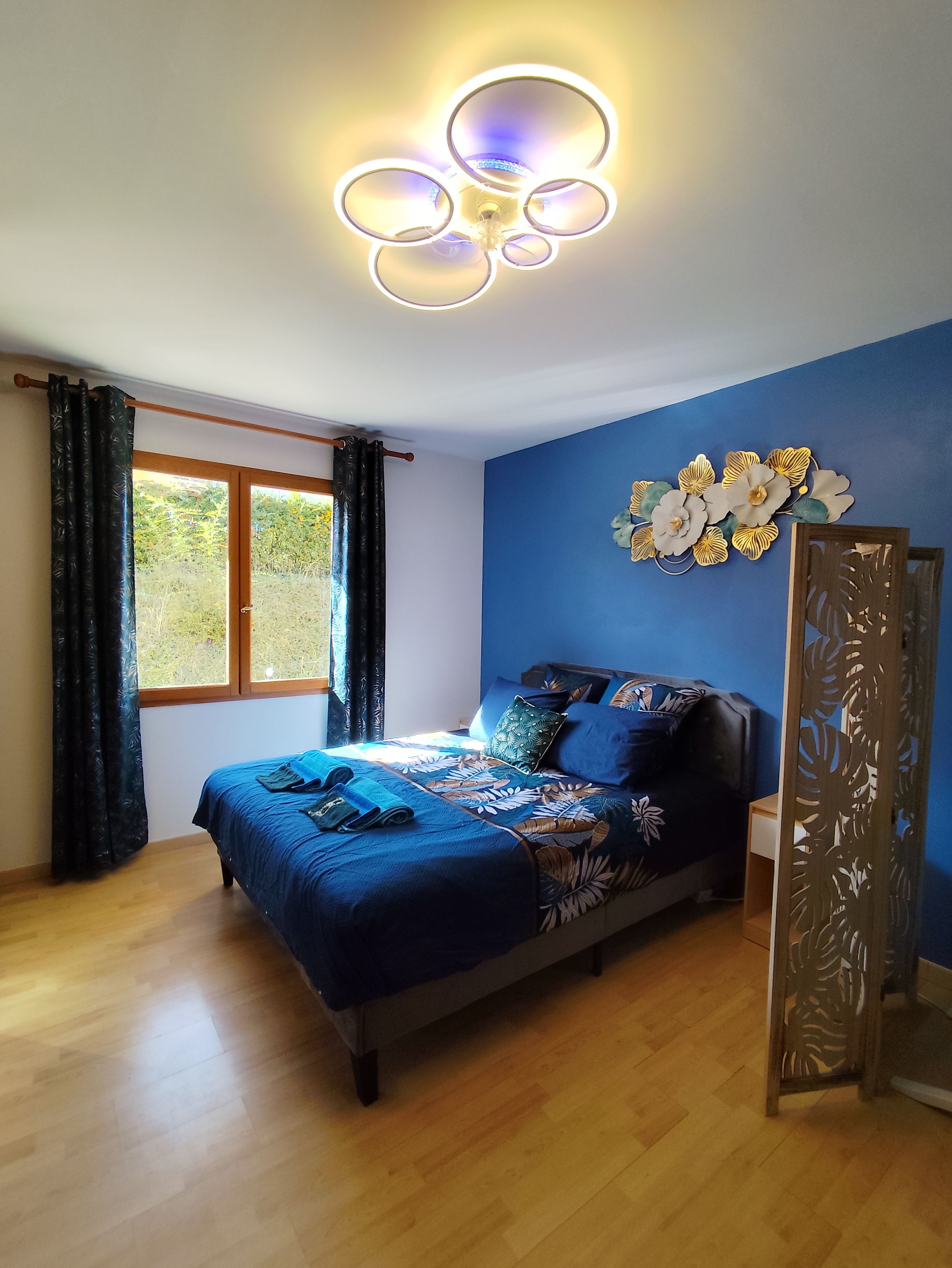 A bedroom with a bed, curtains, a window, and a decorative wall piece.