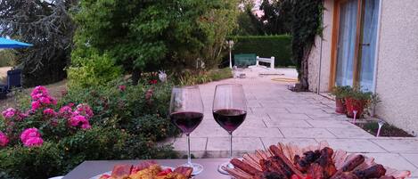 Un espacio al aire libre con comedor, una mesa dispuesta para dos personas, con diversos cortes de carne a la parrilla y una copa de vino tinto.