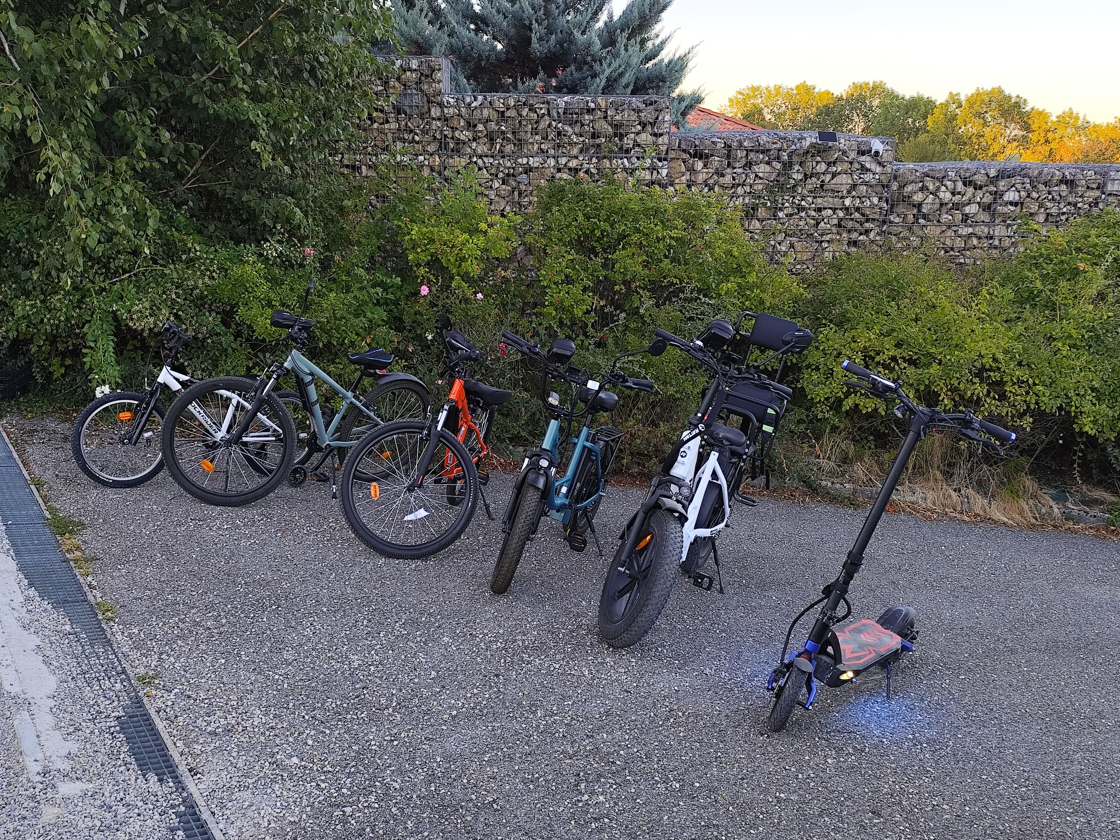 Ein Kiesparkplatz mit Fahrrädern und einem Elektroroller.