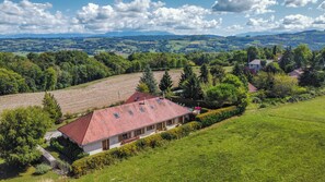 A house with a red roof, surrounded by green fields and trees, with a view of distant hills. - New Listing (Chélieu)