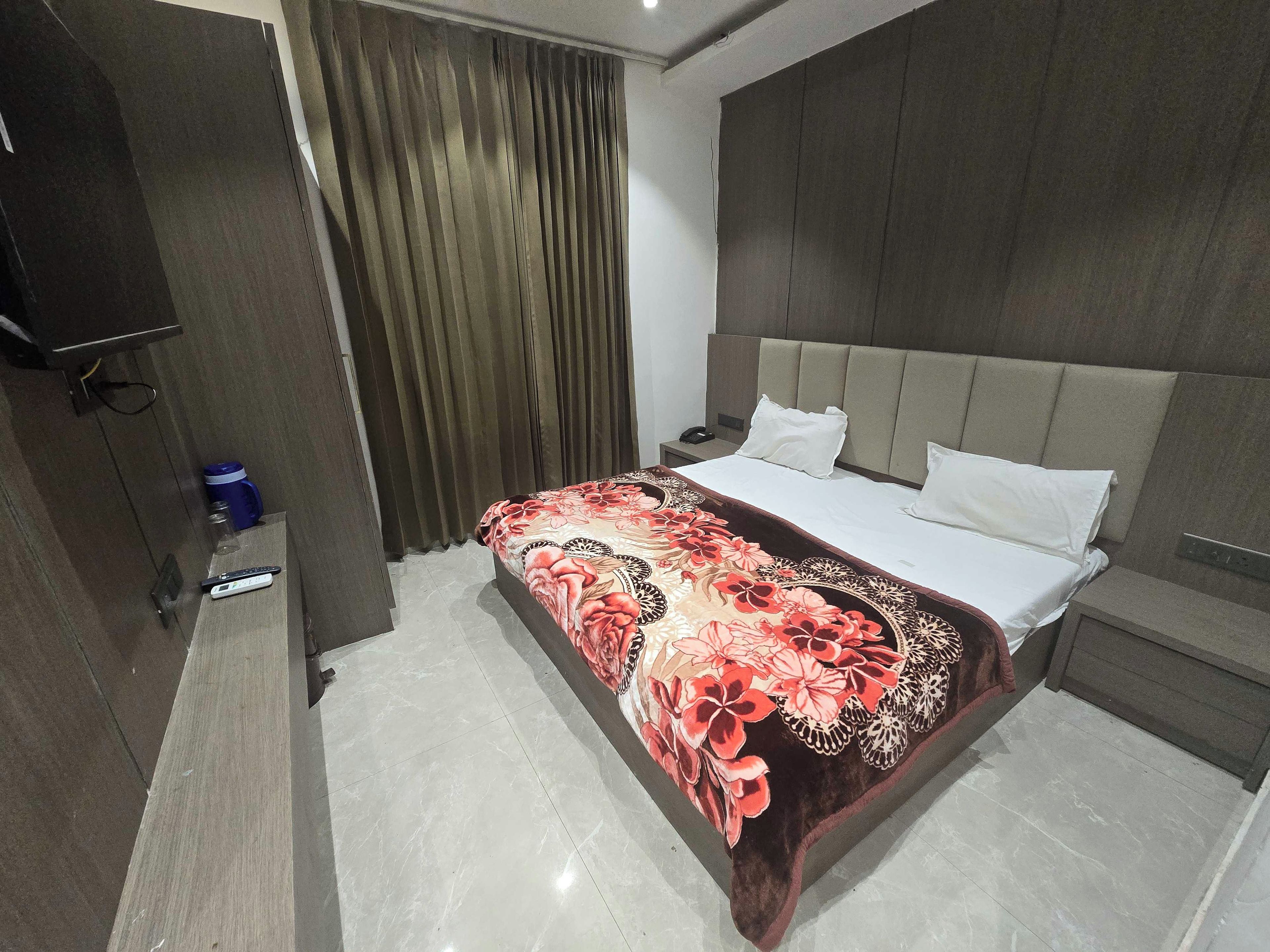 A hotel room with a bed, a nightstand, a television, and a curtain.