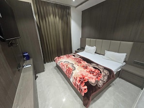 A hotel room with a bed, a nightstand, a television, and a curtain.