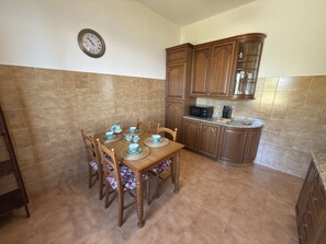 Une cuisine équipée d’une table à manger pour quatre personnes, de meubles de rangement en bois, d’un four à micro-ondes et d’une horloge murale.