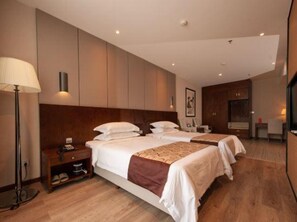 A hotel room with two beds, a nightstand, a lamp, and a large mirror. - Xinhua Hotel Chongqing Kaizhou (Chongqing)