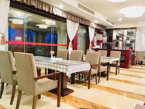 A hotel dining area with tables and chairs, a bar area, and a view through a large window. - Xinhua Hotel Chongqing Kaizhou (Chongqing)