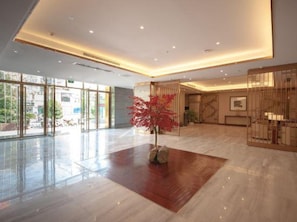 A spacious lobby with a polished floor, a central red plant, and a large glass entrance. - Xinhua Hotel Chongqing Kaizhou (Chongqing)