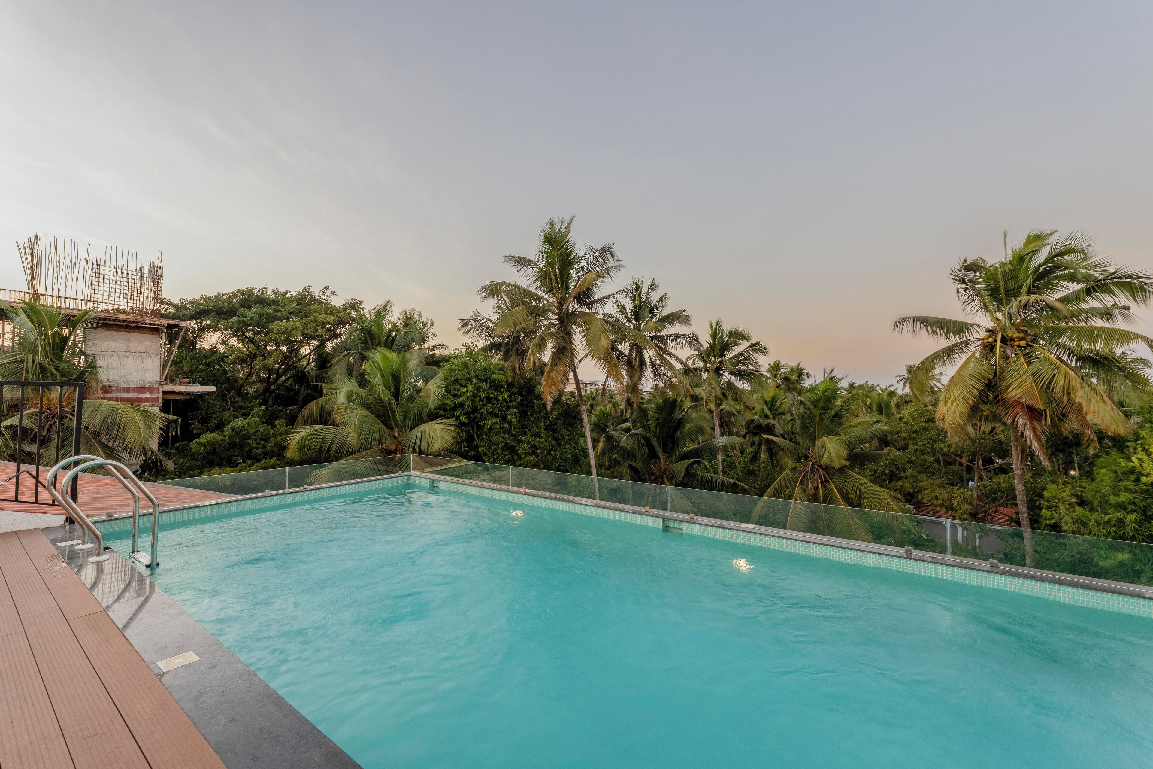 A swimming pool with a wooden deck and metal railings, surrounded by palm trees and greenery.