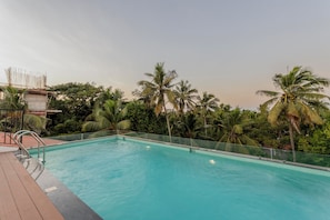 A swimming pool with a wooden deck and metal railings, surrounded by palm trees and greenery.