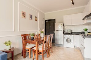 A compact kitchen with a washing machine, a microwave, and a dining area with wooden chairs and a table.