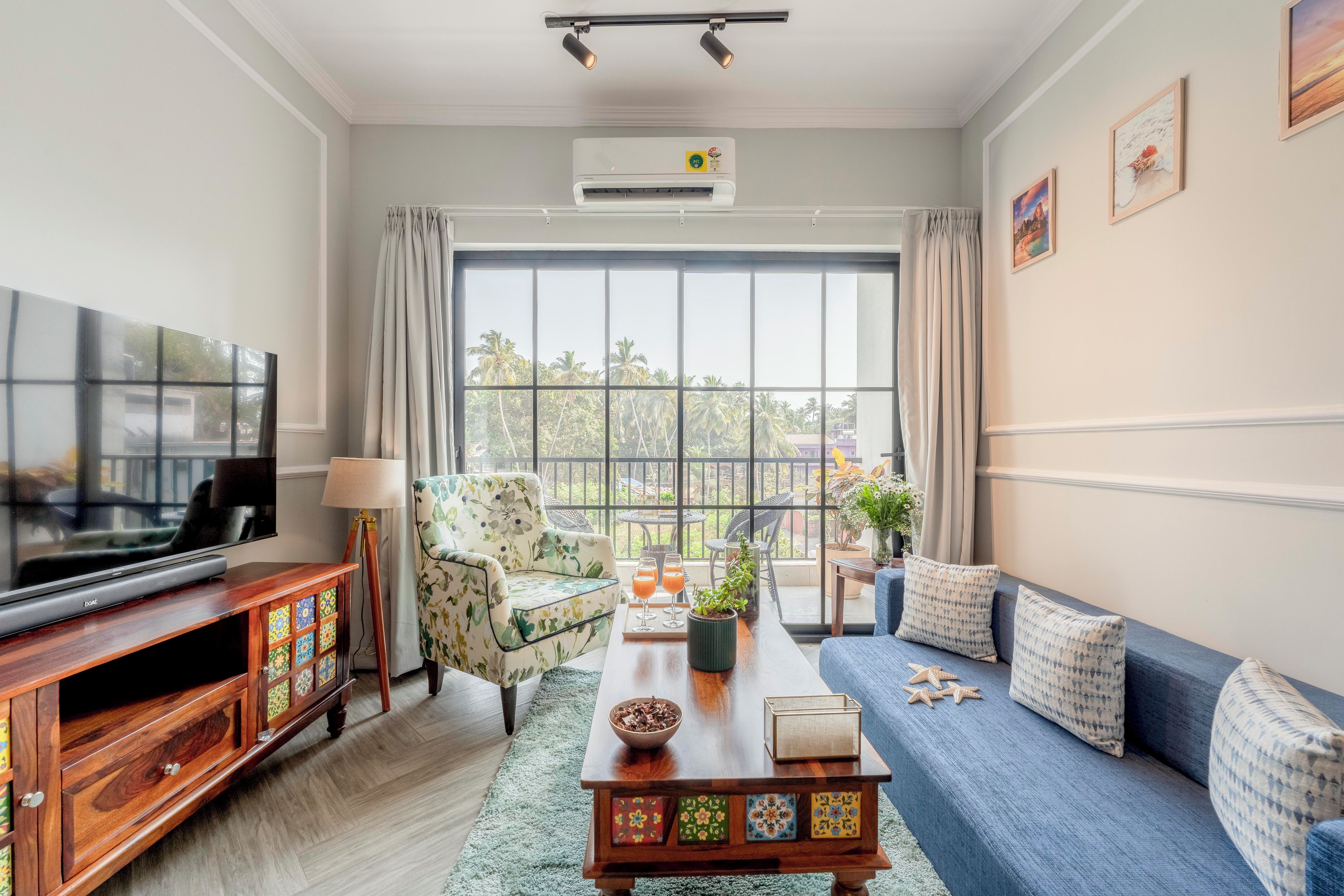 Una sala de estar con televisión, sofá y un amplio ventanal con cortinas.