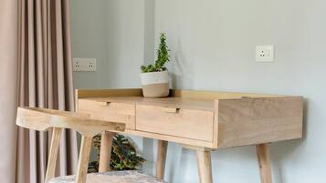 Un escritorio de madera con una planta, una silla y una cortina en una habitación con piso de color claro.