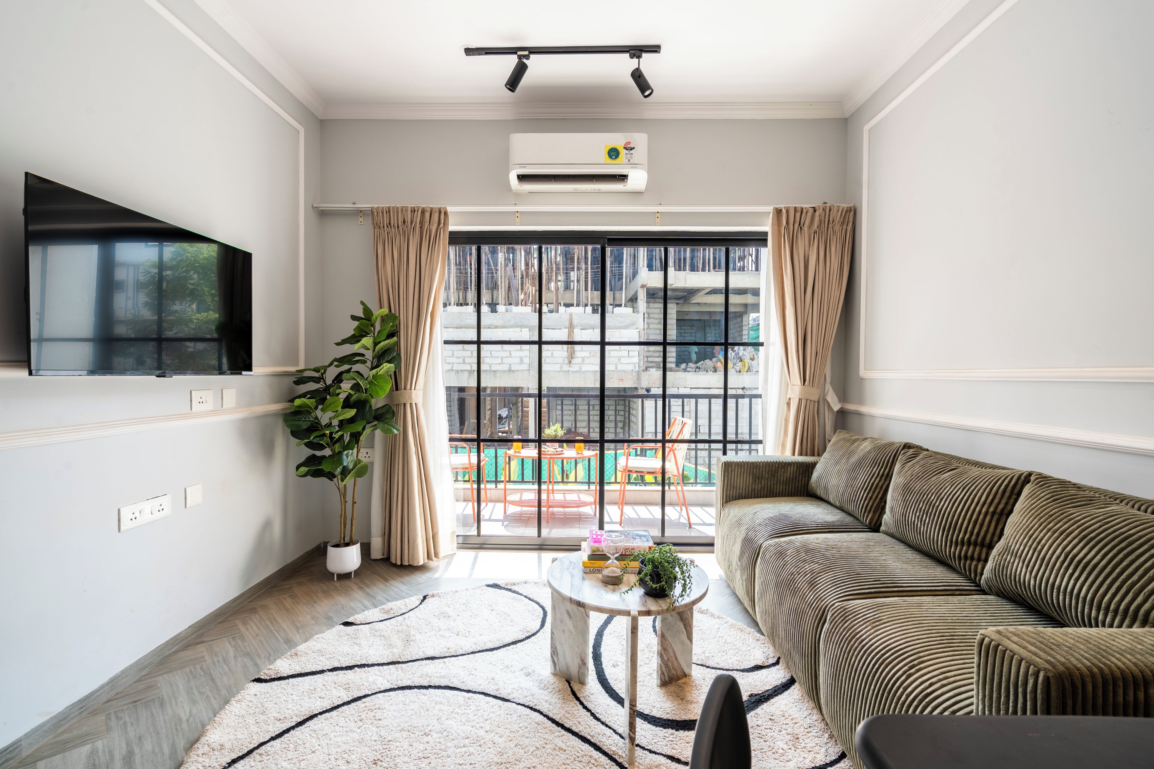 A living room with a sofa, a coffee table, a potted plant, and a large window with curtains.