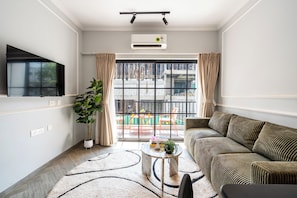 A living room with a sofa, a coffee table, a potted plant, and a large window with curtains.