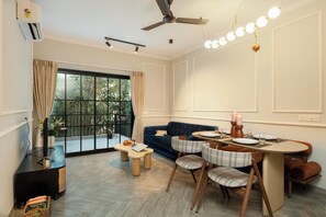 A modern living room with a sofa, dining table, and chairs, a ceiling fan, and a large window with curtains.