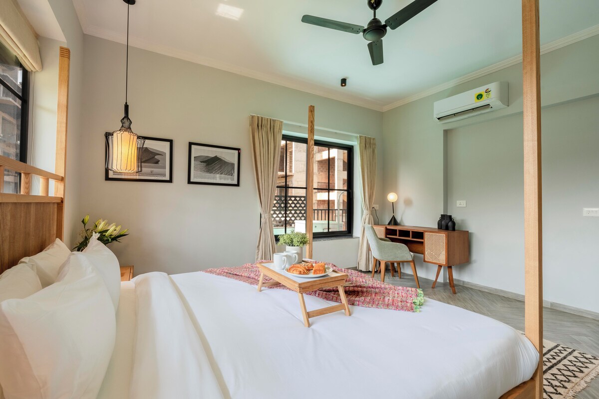 A hotel room with a bed, a desk, a ceiling fan, and a window with curtains.