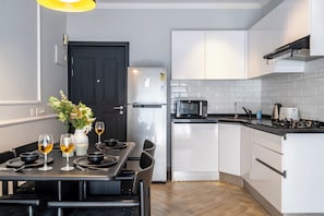 A modern kitchen with white cabinets, a black refrigerator, a microwave, and a gas stove. - Staymaster Avtara - Serviced Apartments (Calangute)