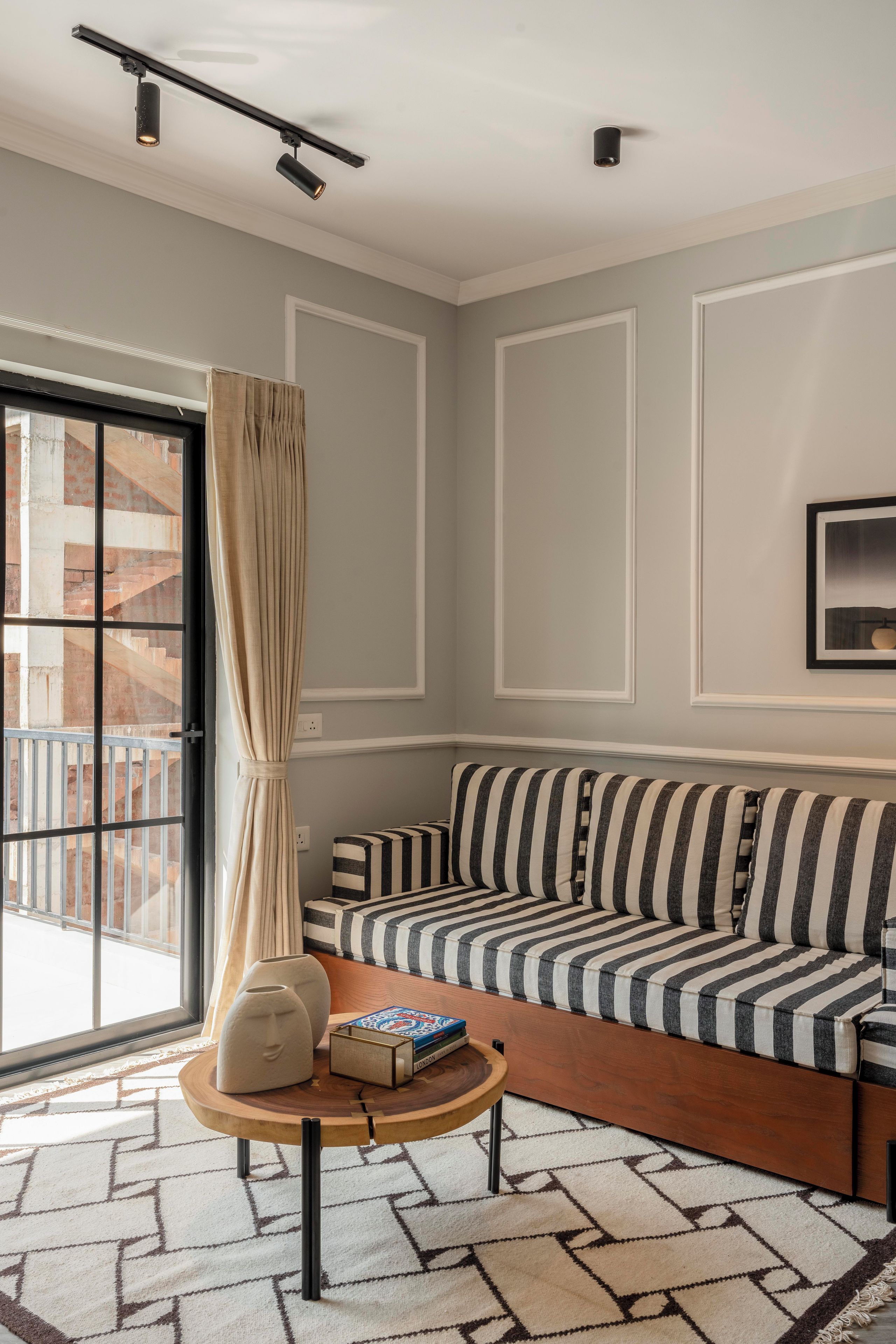 Una sala de estar moderna con un sofá a rayas, una mesa de centro de madera y un amplio ventanal con cortinas.