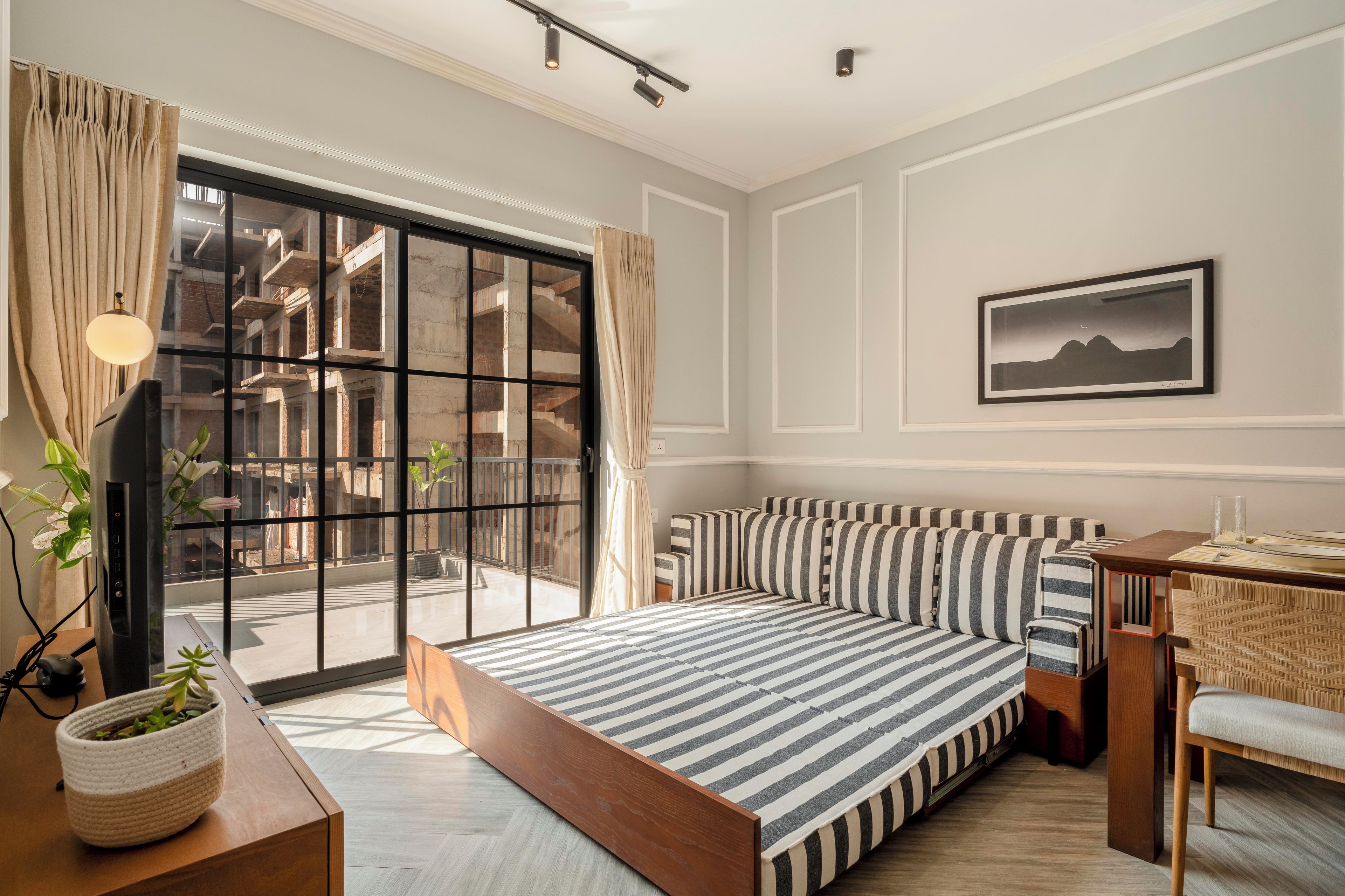 Un dormitorio moderno con una cama grande, un escritorio y vista a un edificio en construcción a través de una puerta de cristal.