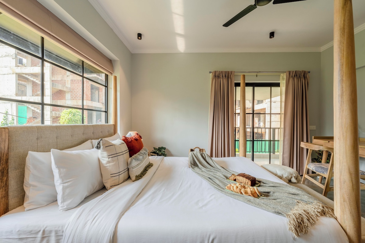 A hotel room with a large bed, a ceiling fan, and a view of buildings through the window.
