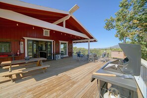Una terraza de madera con mesas y sillas de picnic, una parrilla y un área cubierta con techo rojo.