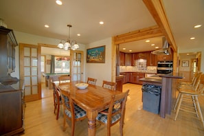 A spacious dining area with a wooden table and chairs, a kitchen with wooden cabinets, and a view of the outdoors through a door. - Spacious Beautiful Country Home on 8 Private Acres (Kelseyville)