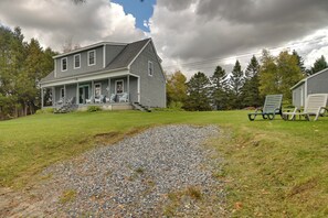 A two-story house with a porch, a gravel driveway, and a grassy yard. - Caspian Lakefront Home w/ Dock and Private Beach (Greensboro)
