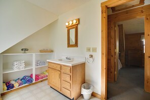 A bathroom with a wooden vanity, a mirror, and a shelf with towels. - Caspian Lakefront Home w/ Dock and Private Beach (Greensboro)