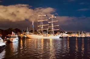 Ein großes Segelschiff liegt in einer Marina vor Anker, mit weiteren Booten und einer Stadtkulisse im Hintergrund.