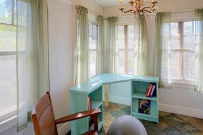 Ein Zimmer mit einem türkisblauen Schreibtisch, einem Stuhl, einem Bücherregal und einem Fenster mit Vorhängen.