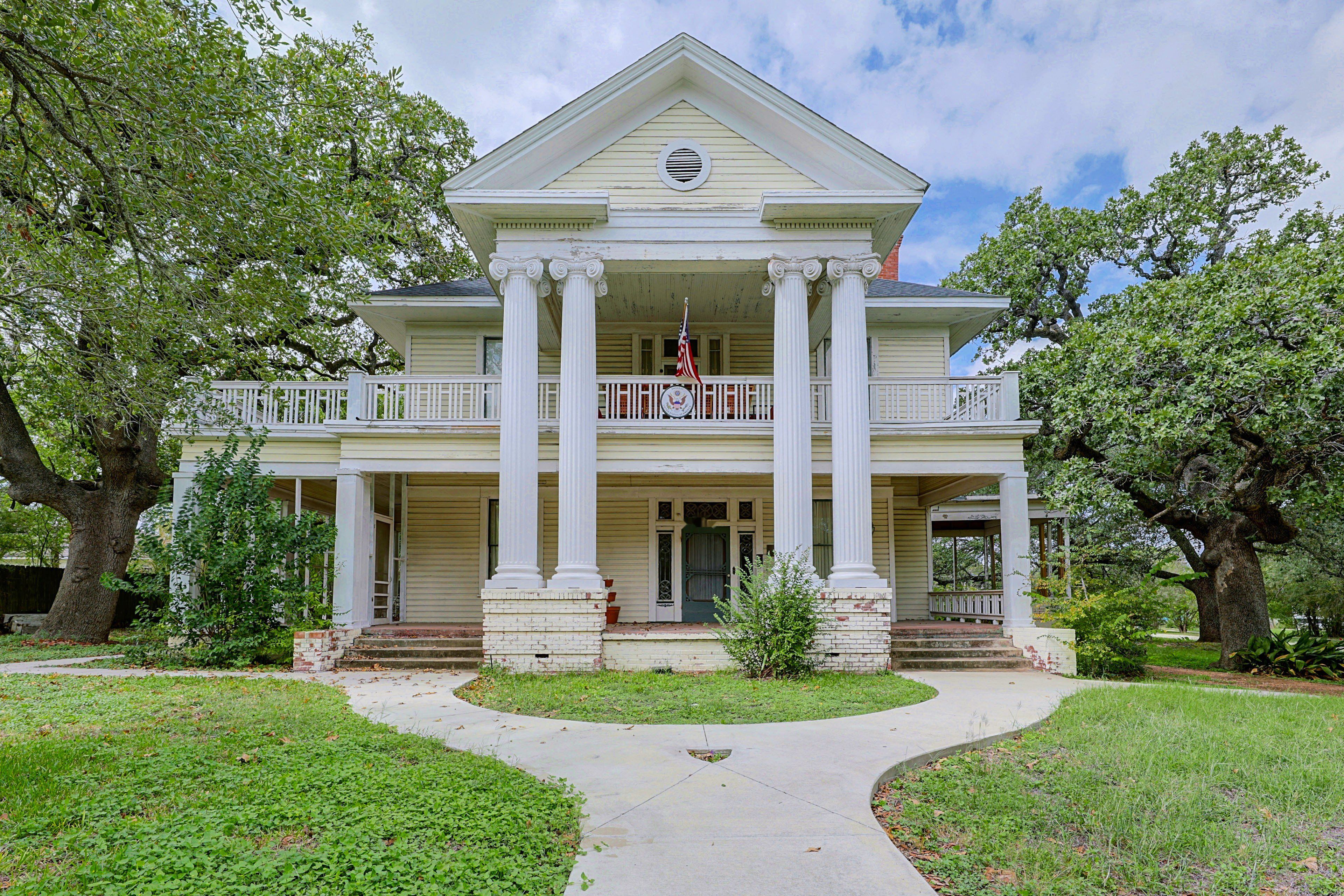 A two-story building with a central entrance, flanked by large columns, and a balcony with railings.