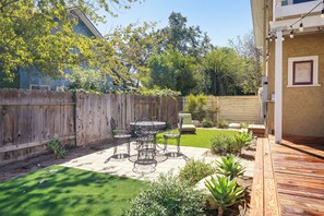 A backyard with a wooden deck, a metal table with chairs, a small lawn, and a wooden fence.