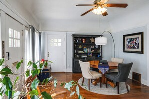 A dining area with a round table, chairs, a bookshelf, and a ceiling fan.