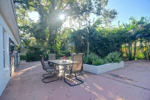 Eine Terrasse im Freien mit Tisch und Stühlen, umgeben von üppigem Grün und einer weißen Wand.