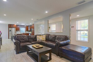 A living room with a brown leather sectional sofa, a coffee table, and a kitchen in the background. - Near ZooTampa & Buccaneers Games! Modern Retreat (Tampa)