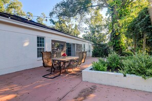 A patio with a table and chairs, surrounded by a garden and trees. - Near ZooTampa & Buccaneers Games! Modern Retreat (Tampa)