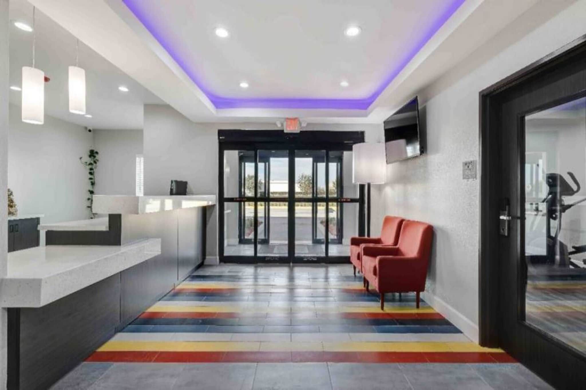Zona de recepción con diseño moderno, que incluye un mostrador de recepción, un espacio de asientos con sillas rojas y un piso con rayas coloridas.
