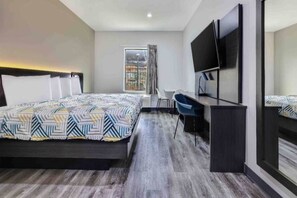 Una habitación de hotel con cama, escritorio, silla, televisor y ventana con cortinas.