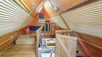An attic bedroom with a wooden sloped ceiling, a small window, and a built-in heater.