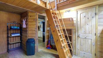 Un interno in legno con una scala che conduce a un livello superiore, un mobiletto a scaffali in metallo e una porta.