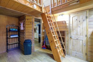 Un interno in legno con una scala che conduce a un livello superiore, un mobiletto a scaffali in metallo e una porta.