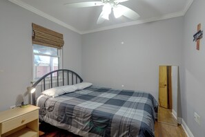 Una camera da letto con un letto, un comodino, una lampada, una finestra con vista, un ventilatore a soffitto e una porta.